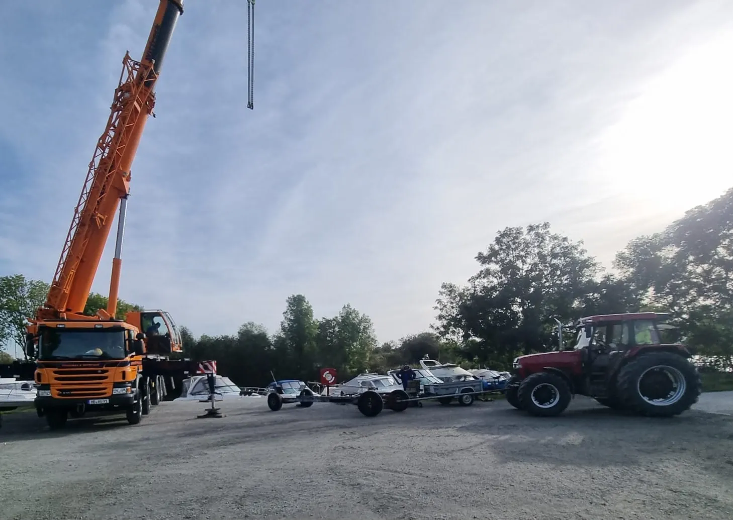 Ein orangefarbener Mobilkran und ein Traktor mit Bootstrailer stehen auf dem Lagerplatz bereit