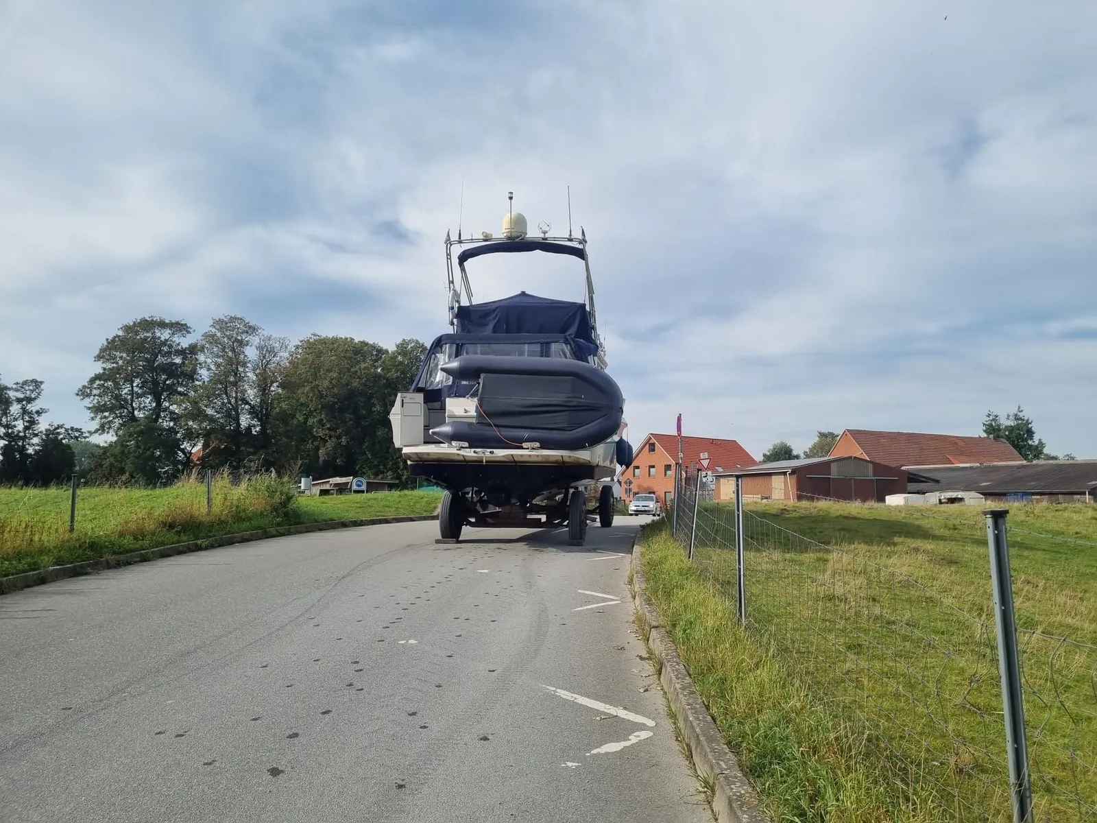 Eine Motoryacht mit Persenning und Beiboot wird auf einem Hafentrailer über eine Straße gezogen