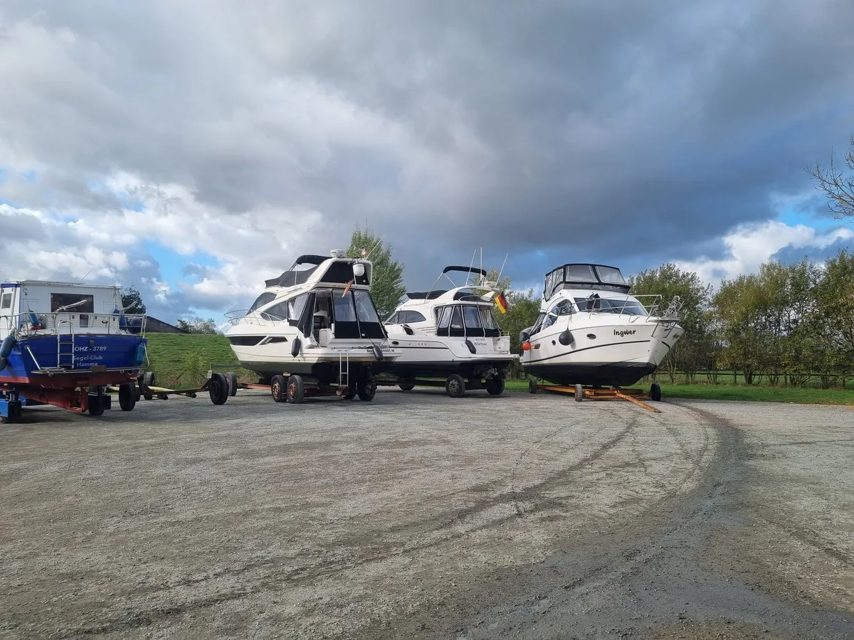 Drei Motoryachten und ein blaues Motorboot stehen auf Hafentrailern auf dem Lagerplatz, darüber dunkle Wolken