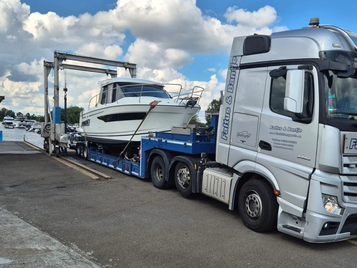 Eine weiße Motoryacht steht festgezurrt auf dem Tieflader eines Yachttransporters, dahinter der Hafenlift