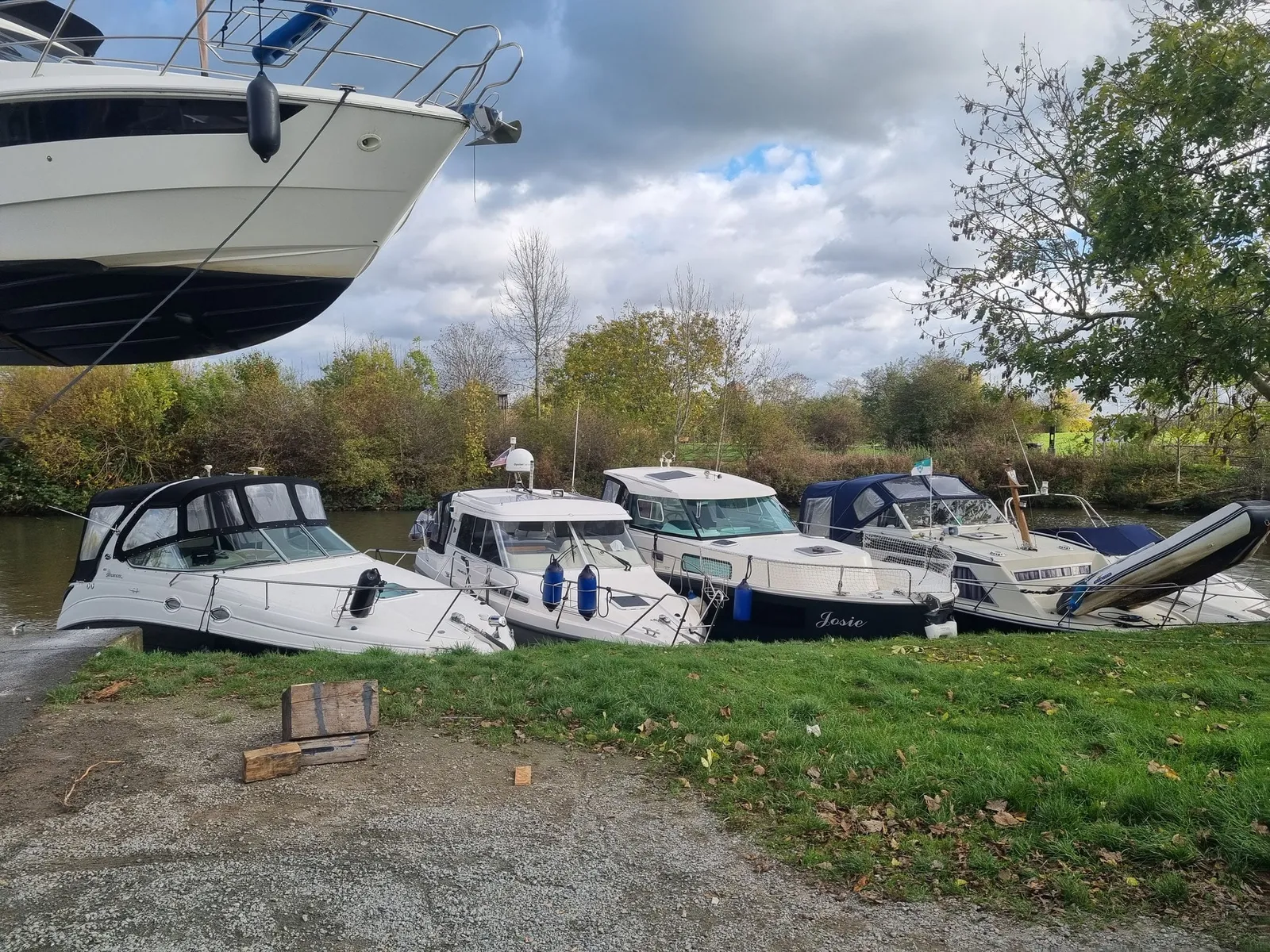 Der Bug einer Motoryacht hängt am Kran, darunter liegen vier Sportboote am Ufer